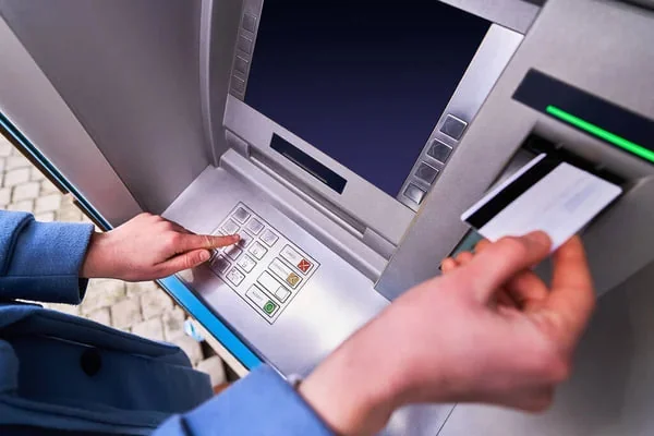 Osoba korzysta z bankomatu, naciskając przyciski i trzymając kartę przy czytniku.