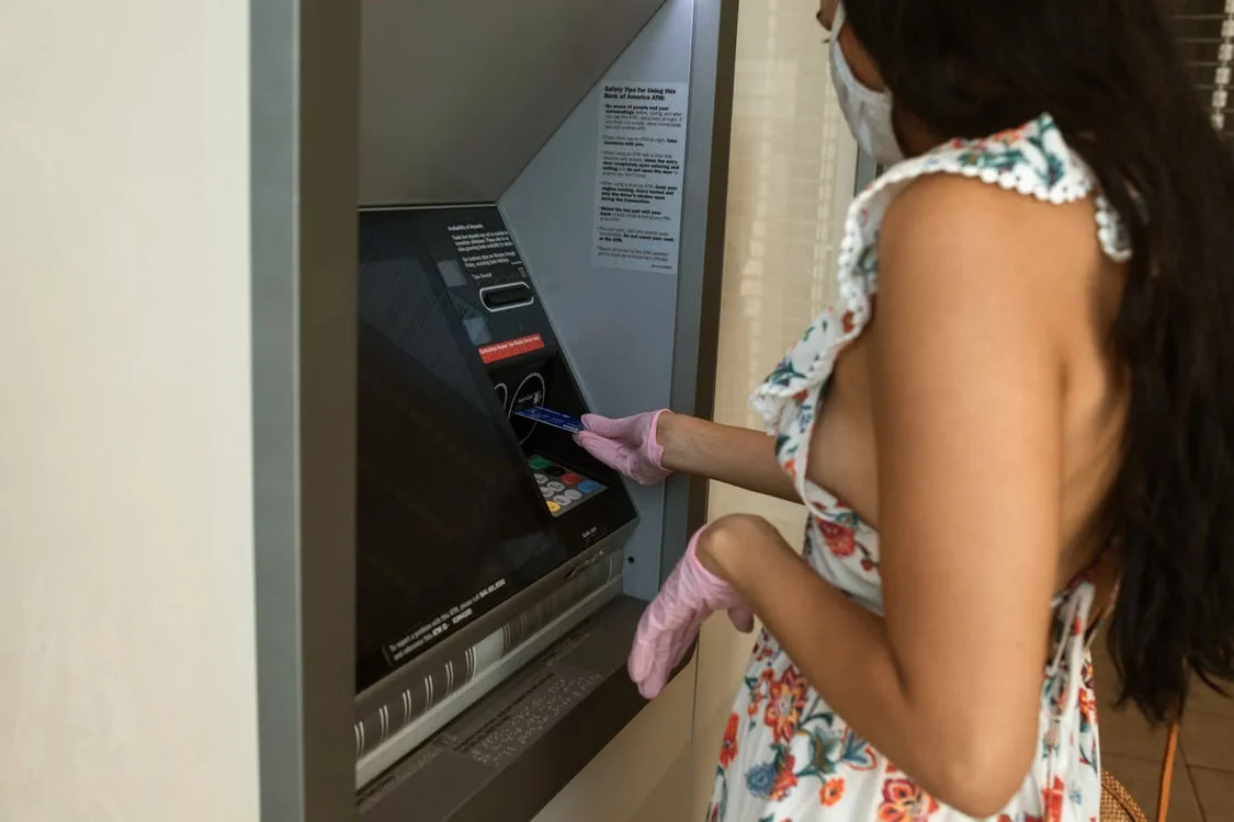 Kobieta w maseczce korzysta z bankomatu wewnątrz placówki bankowej.